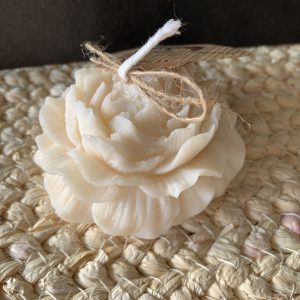 Bougie moulée en forme de pivoine couleur ivoire, finition fleur détaillée, posée sur un tapis tressé naturel avec ficelle et étiquette.